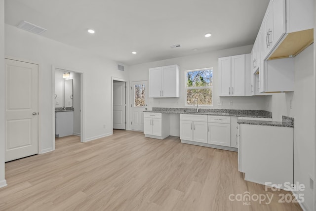 kitchen with recessed lighting, light wood-style flooring, white cabinets, a sink, and dark stone countertops