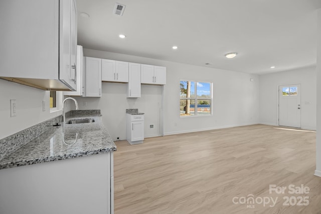 kitchen with visible vents, white cabinets, light stone counters, light wood-type flooring, and a sink