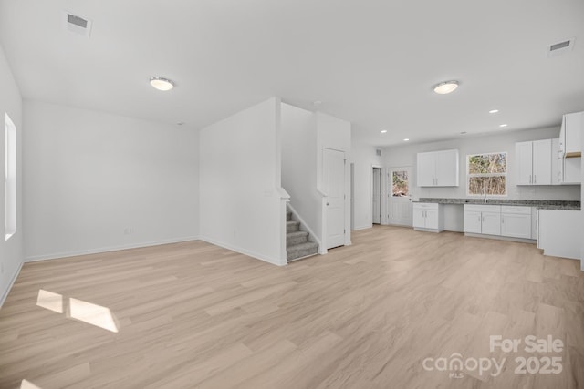 unfurnished living room featuring stairway, light wood-type flooring, a sink, and visible vents