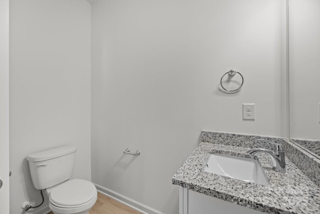 bathroom with wood finished floors, vanity, toilet, and baseboards