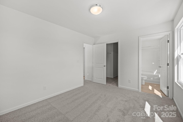 unfurnished bedroom with baseboards, a walk in closet, carpet flooring, and ensuite bathroom