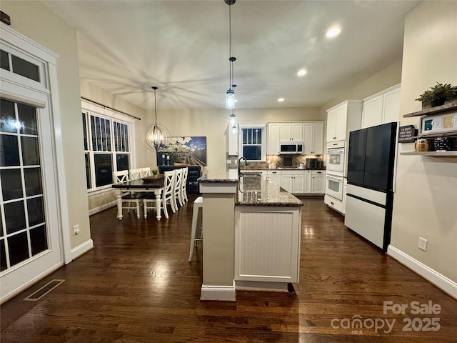 kitchen with a sink, white cabinets, freestanding refrigerator, dark stone counters, and pendant lighting