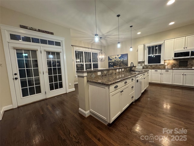 kitchen featuring white cabinets, dishwasher, dark stone countertops, hanging light fixtures, and a sink