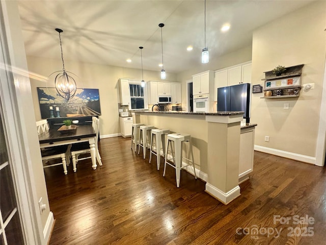 kitchen featuring a breakfast bar, white oven, hanging light fixtures, freestanding refrigerator, and white cabinets