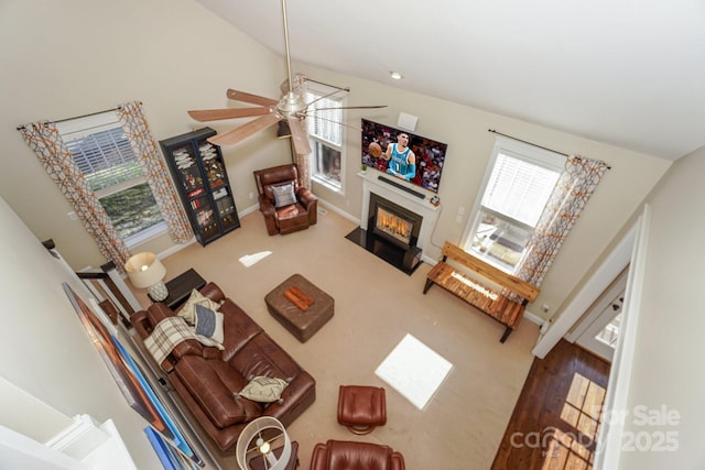 carpeted living room featuring lofted ceiling, a fireplace with flush hearth, baseboards, and a ceiling fan