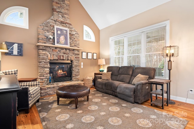 living room with wood-type flooring, a stone fireplace, and a healthy amount of sunlight