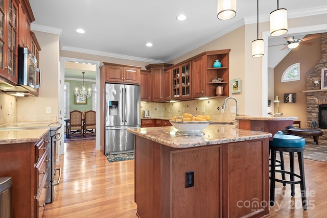 kitchen with a breakfast bar, hanging light fixtures, kitchen peninsula, stainless steel appliances, and light stone countertops