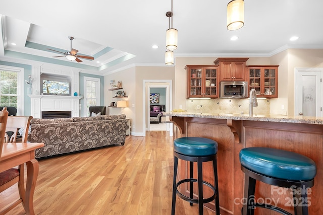 kitchen featuring crown molding, light hardwood / wood-style flooring, light stone countertops, decorative light fixtures, and a raised ceiling