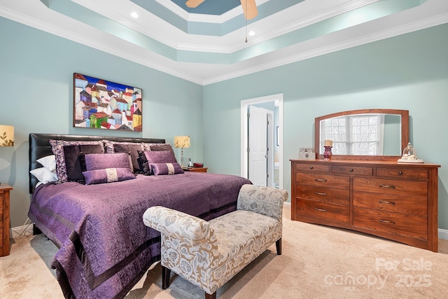 carpeted bedroom with a tray ceiling, ensuite bath, ornamental molding, and ceiling fan