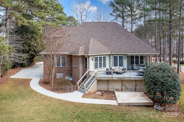 rear view of property with a yard, a shingled roof, a deck, brick siding, and stairs