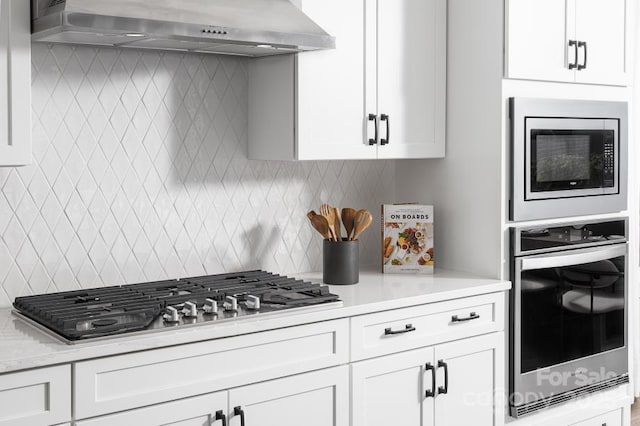 kitchen featuring tasteful backsplash, appliances with stainless steel finishes, wall chimney range hood, and white cabinetry