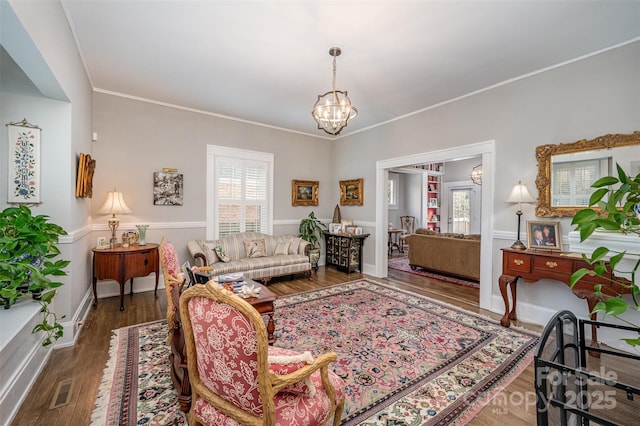 living room with dark wood-type flooring, a healthy amount of sunlight, crown molding, and a notable chandelier