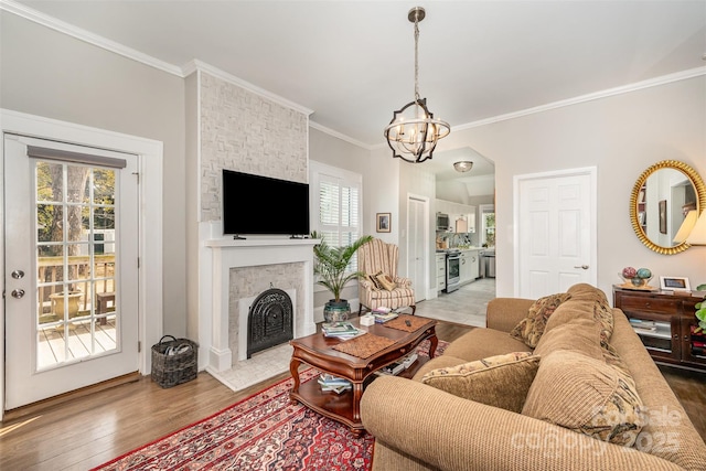 living room featuring crown molding, a stone fireplace, a chandelier, and light wood-type flooring