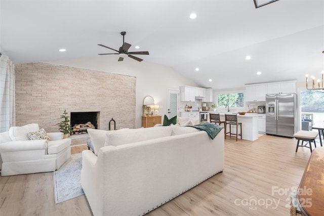 living room with vaulted ceiling, ceiling fan with notable chandelier, a fireplace, and light hardwood / wood-style floors