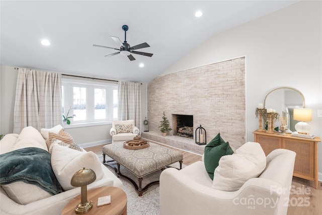 living room with ceiling fan, a fireplace, vaulted ceiling, and light hardwood / wood-style flooring