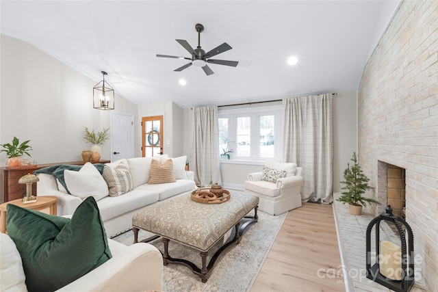 living room featuring lofted ceiling, a brick fireplace, light hardwood / wood-style floors, and ceiling fan