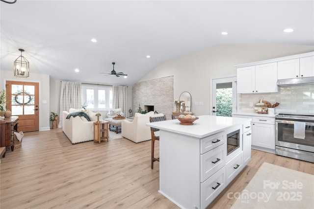 kitchen featuring decorative light fixtures, lofted ceiling, white cabinets, stainless steel appliances, and light wood-type flooring