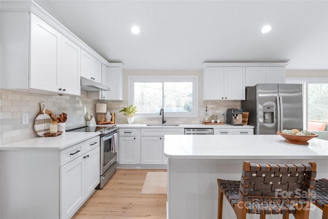 kitchen featuring sink, light hardwood / wood-style flooring, white cabinetry, stainless steel appliances, and tasteful backsplash