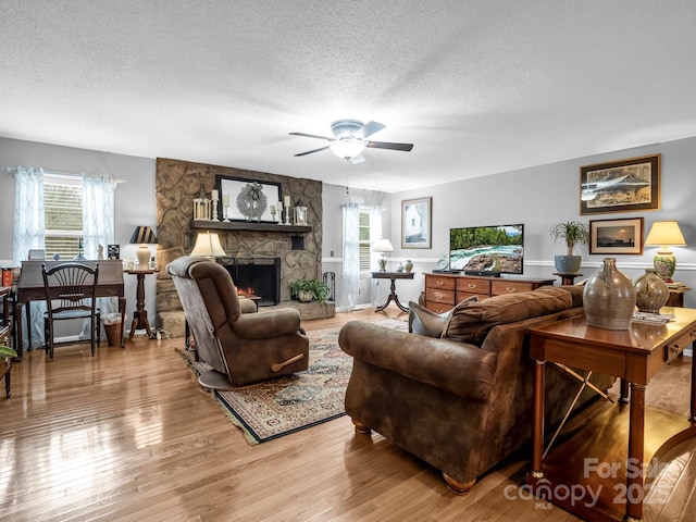 living room with ceiling fan, a fireplace, light hardwood / wood-style floors, and a textured ceiling