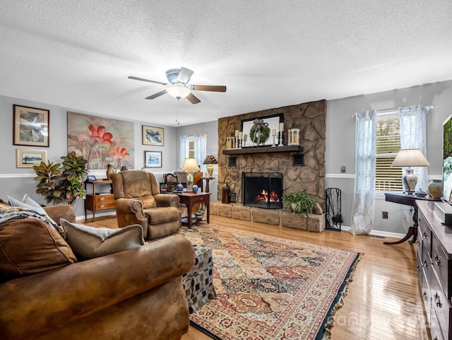 living room with a textured ceiling, a fireplace, ceiling fan, and light wood-type flooring