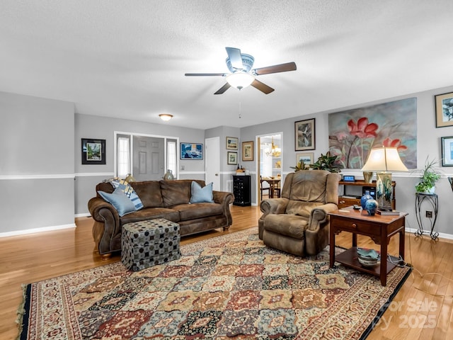 living room with hardwood / wood-style flooring, ceiling fan with notable chandelier, and a textured ceiling