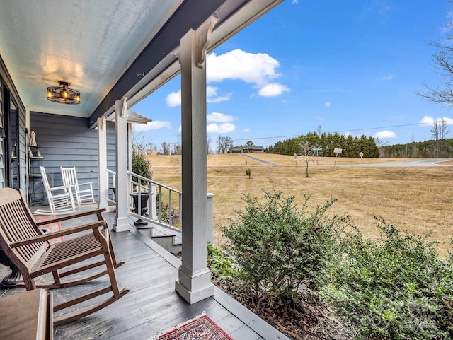 wooden deck with a rural view, a lawn, and covered porch