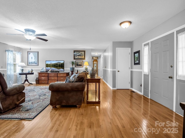 living room featuring ceiling fan, a textured ceiling, and light hardwood / wood-style floors