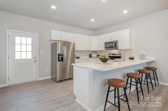 kitchen with sink, white cabinetry, appliances with stainless steel finishes, a kitchen breakfast bar, and kitchen peninsula