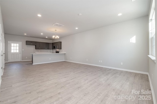 unfurnished living room with a notable chandelier and light hardwood / wood-style floors