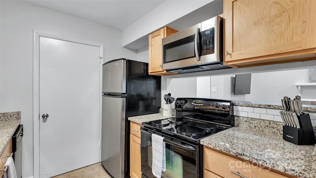 kitchen with light tile patterned floors, light brown cabinets, appliances with stainless steel finishes, and light stone counters