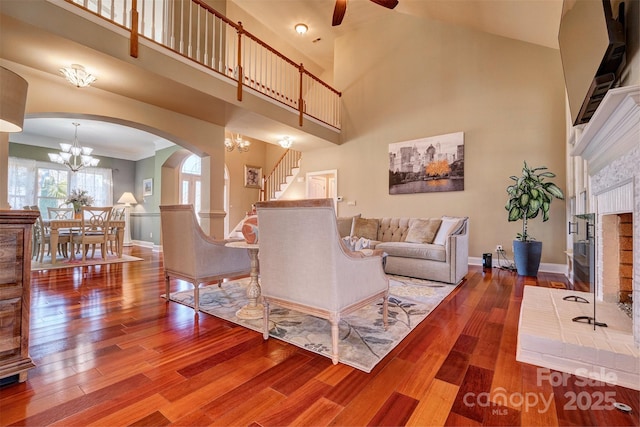 living room with hardwood / wood-style flooring, ceiling fan with notable chandelier, and a high ceiling