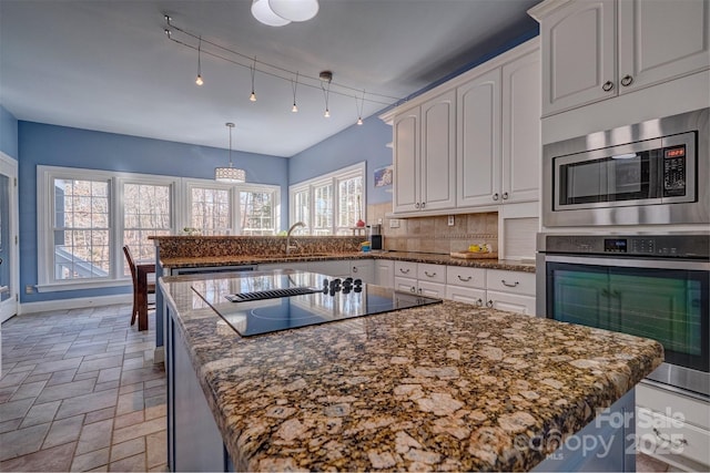 kitchen featuring appliances with stainless steel finishes, decorative light fixtures, a center island, and white cabinets