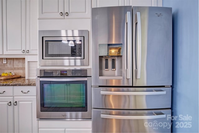 kitchen with stainless steel appliances, white cabinetry, backsplash, and dark stone counters