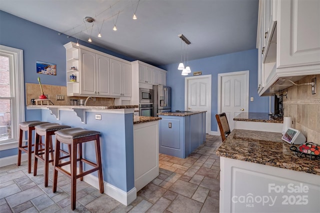 kitchen with appliances with stainless steel finishes, white cabinetry, a center island, decorative light fixtures, and kitchen peninsula