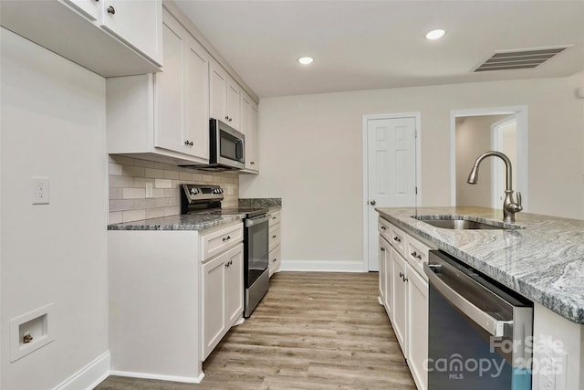 kitchen with tasteful backsplash, sink, white cabinetry, stainless steel appliances, and light stone counters