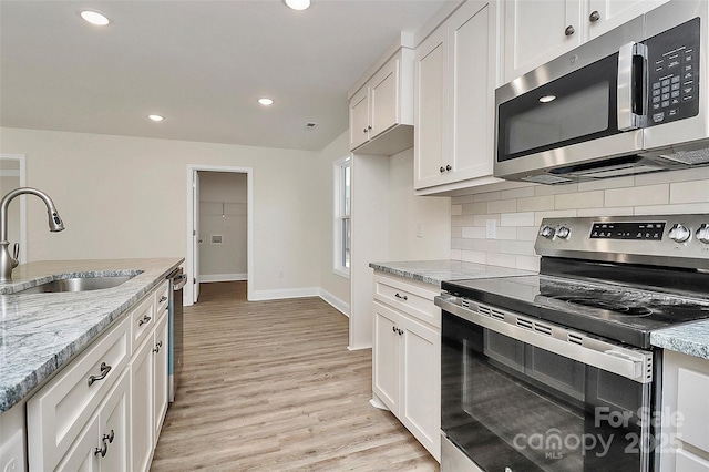 kitchen with white cabinetry, light hardwood / wood-style floors, appliances with stainless steel finishes, light stone countertops, and sink