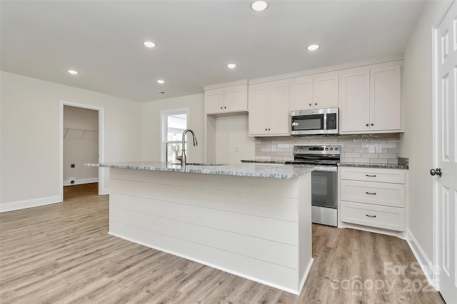 kitchen featuring white cabinetry, stainless steel appliances, sink, backsplash, and a center island with sink