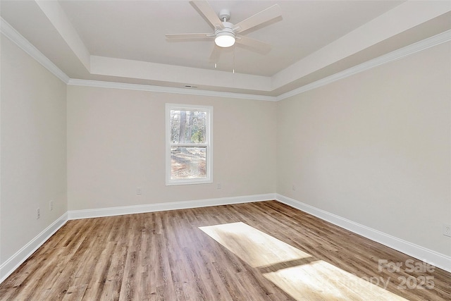 unfurnished room featuring a raised ceiling, light wood-type flooring, crown molding, and ceiling fan