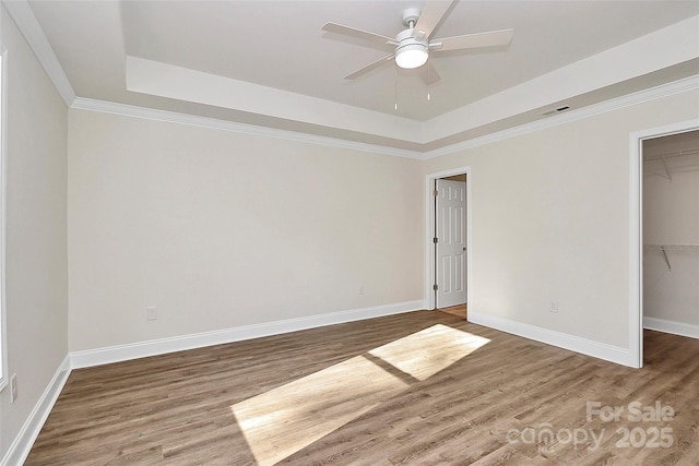 unfurnished bedroom featuring ceiling fan, a walk in closet, a closet, and a tray ceiling