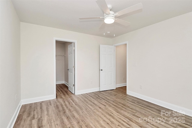 unfurnished bedroom with a spacious closet, ceiling fan, a closet, and light hardwood / wood-style flooring