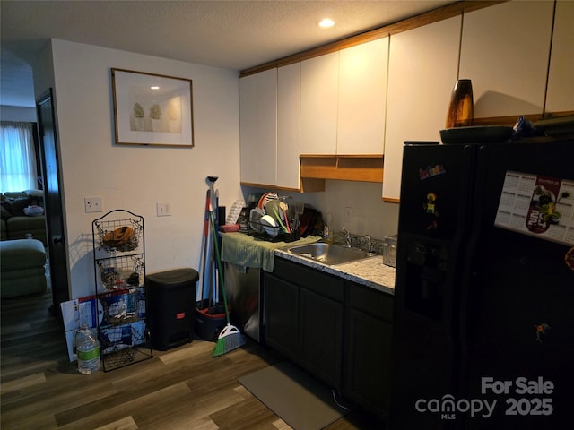 kitchen featuring hardwood / wood-style floors, sink, white cabinets, black fridge, and a textured ceiling