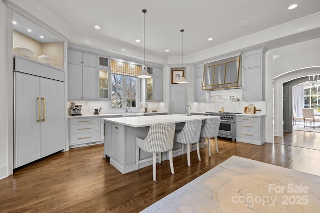 kitchen featuring backsplash, wall chimney range hood, a kitchen island with sink, and high end appliances