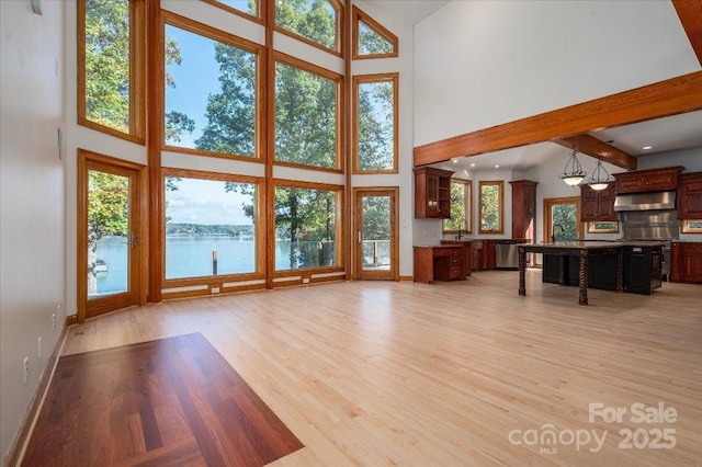 unfurnished living room with a water view, a towering ceiling, and light wood-type flooring