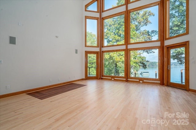 unfurnished living room featuring a water view, light hardwood / wood-style flooring, and a high ceiling