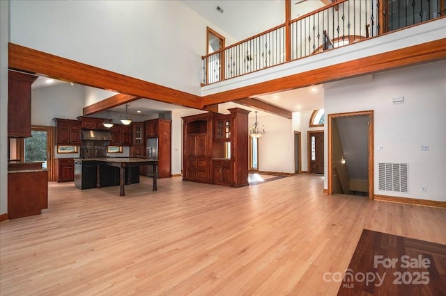 living room with beamed ceiling, a notable chandelier, light wood-type flooring, and a high ceiling