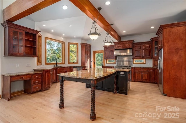 kitchen featuring appliances with stainless steel finishes, hanging light fixtures, beam ceiling, extractor fan, and a center island with sink