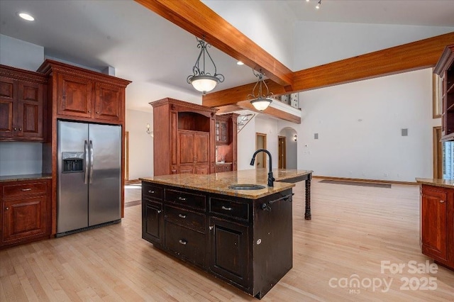 kitchen featuring stainless steel refrigerator with ice dispenser, sink, a kitchen island with sink, beam ceiling, and light hardwood / wood-style floors