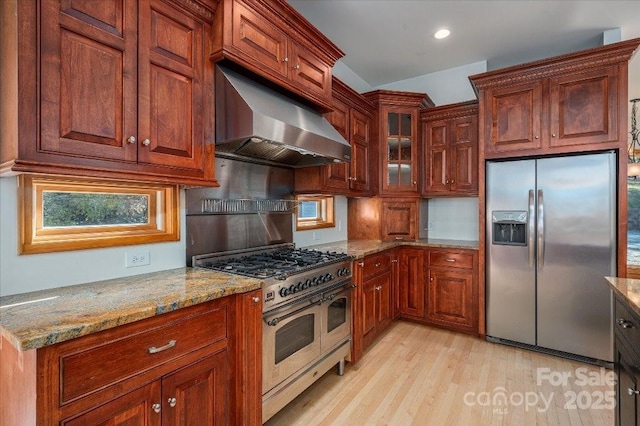 kitchen with light stone counters, stainless steel appliances, range hood, and light wood-type flooring