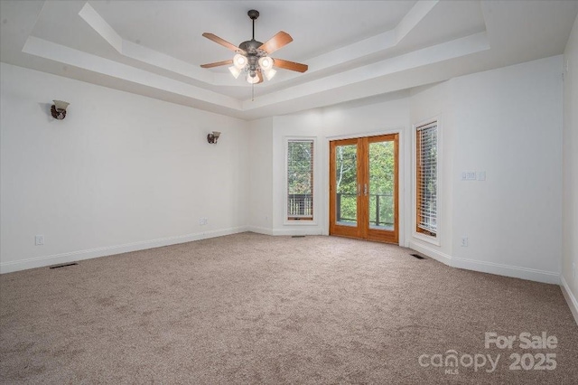 empty room with carpet floors, a raised ceiling, ceiling fan, and french doors