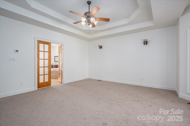 spare room featuring a tray ceiling, light colored carpet, french doors, and ceiling fan